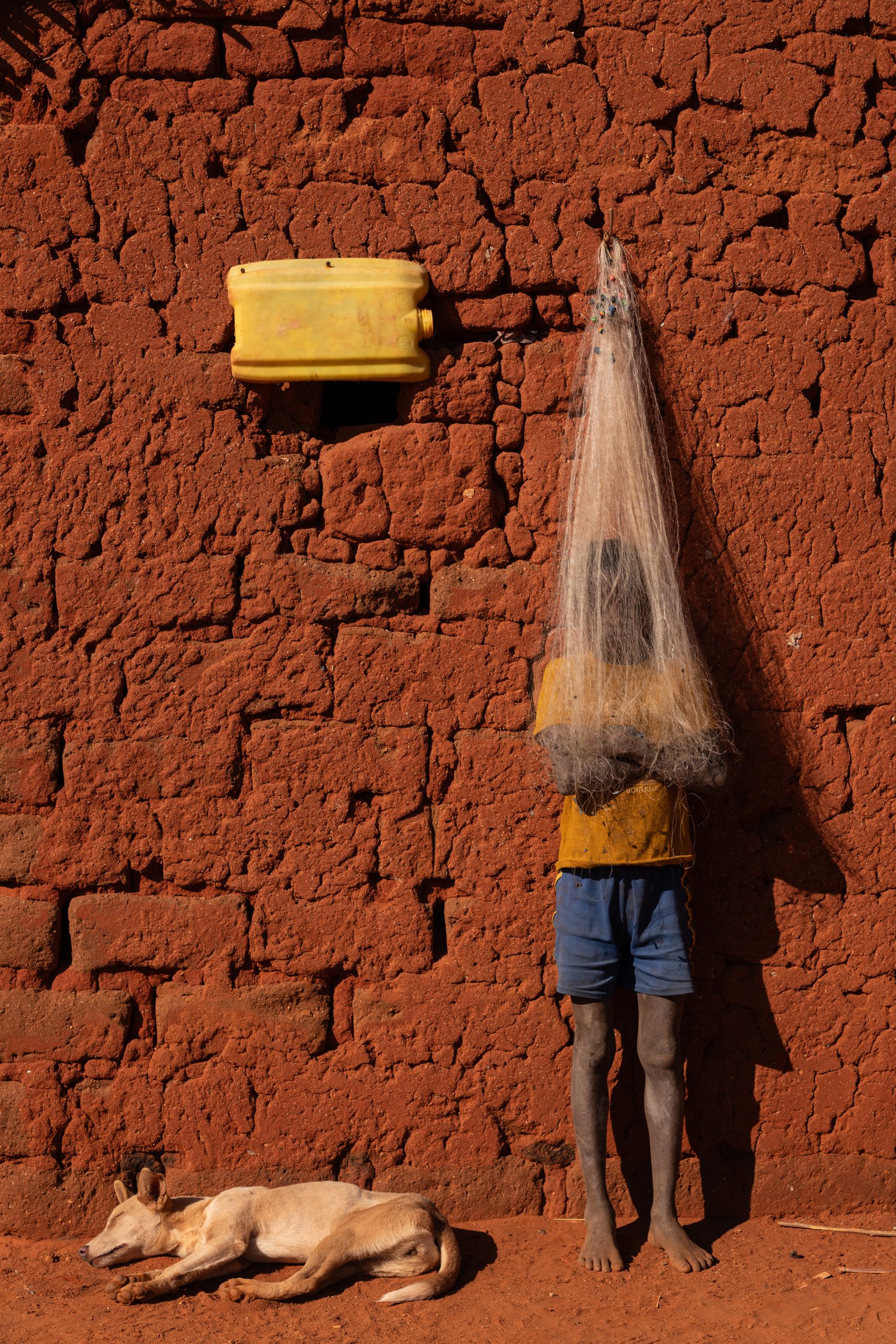 Photo: Lahiandro, a 14-year-old boy, stands behind a fishnet hanging on a wall. Photo credit: Safidy Andrianantenaina