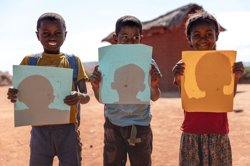 Photo: Lahiandro (14), Mahefa (11), and Mavitrika (6) proudly hold their drawings of the school, a symbol of hope and change in their lives. Photo credit: Safidy Andrianantenaina