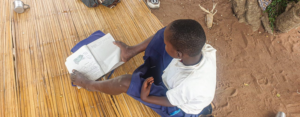 Magaiwa using her feet to read pages of a book, photo credit: ATFGM