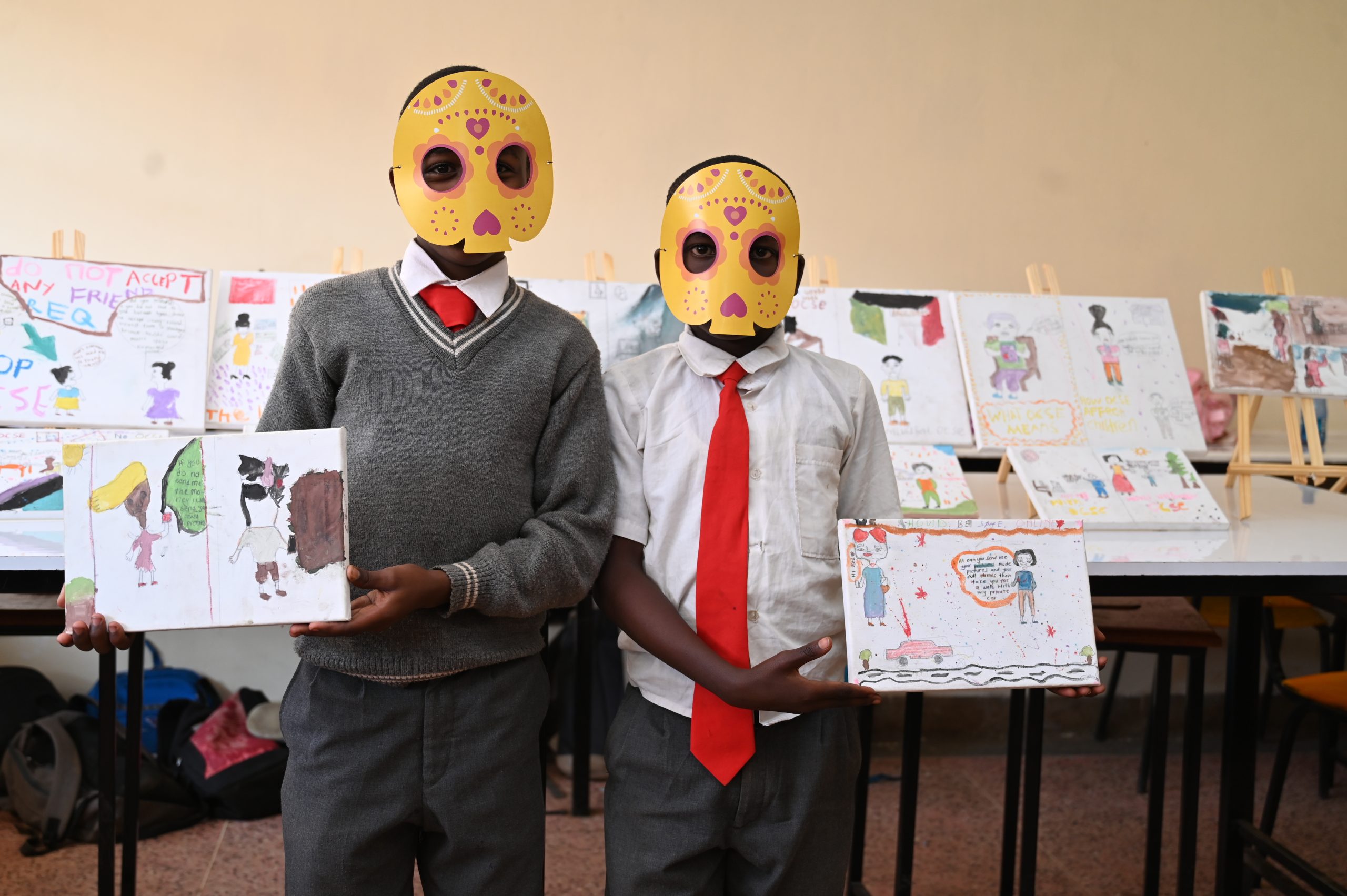 Two children holding drawings with masks on