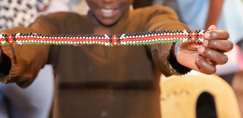 A child holding up a Kenyan Bracelet that he made